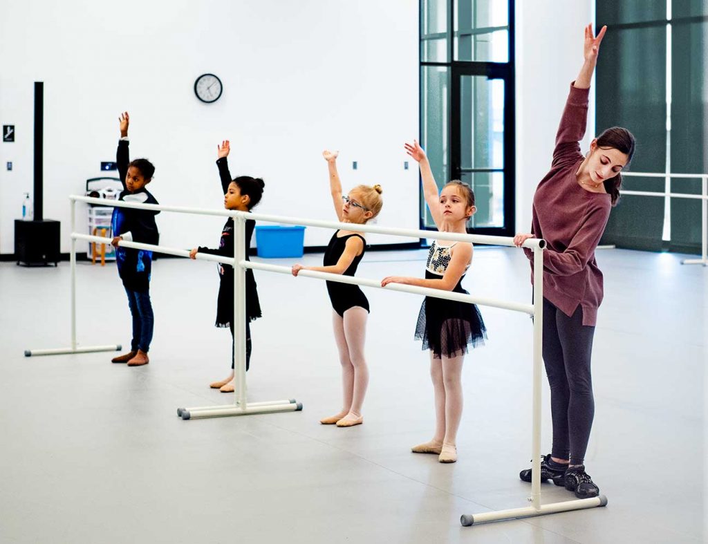 Four young dancers work on posture and positioning at a ballet barre with an American Midwest Ballet instructor.